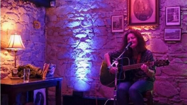 Photo of singer Briege Murphy singing and playing guitar in a club.